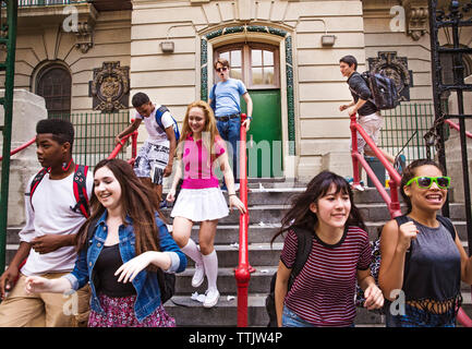 Happy students moving down on steps outside high school Stock Photo