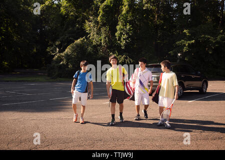 Siblings carrying bags walking on street against parked car and trees Stock Photo