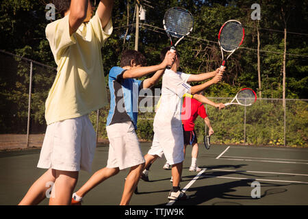 Players standing in row playing tennis against fence at court Stock Photo