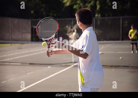 Players playing tennis at court against fence Stock Photo