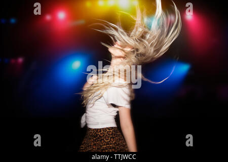 Woman with tousled hair dancing against illuminated multi colored lights at garden party Stock Photo