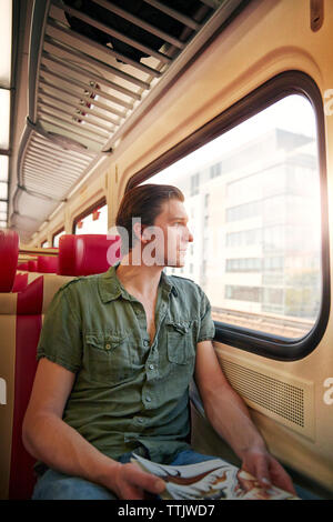 Thoughtful man looking through window while traveling in train Stock Photo