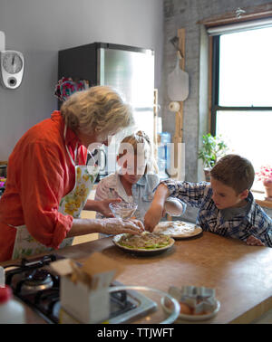 Children with grandmother garnishing food in kitchen Stock Photo