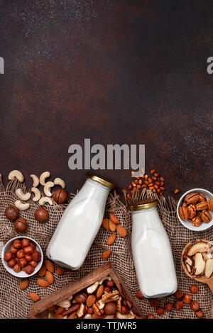 vegetable nut milk in glass bottles, different types of nuts on a dark background. view from above Stock Photo