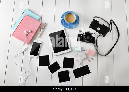 Tablet, phone, photos and cup of coffee on a wooden desk background, top view Stock Photo