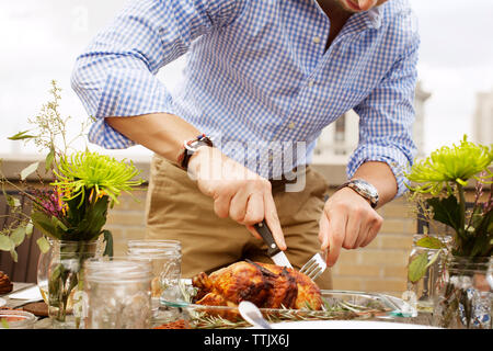 Midsection of man carving roasted chicken at table on building terrace Stock Photo