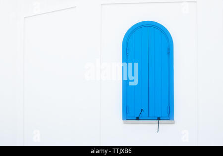 One small arched blue door with metal hinges on a plain white wall Stock Photo