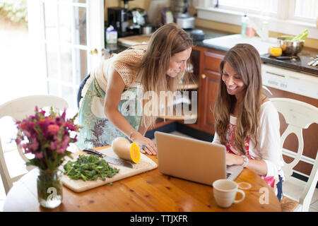 Happy women using laptop computer while preparing food at home Stock Photo