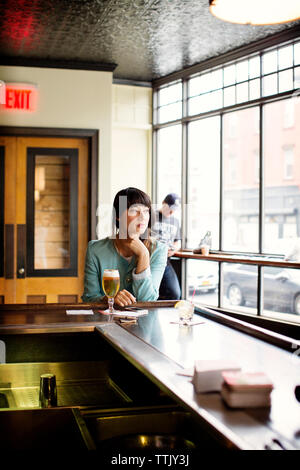 Thoughtful woman looking away while leaning on table in bar Stock Photo
