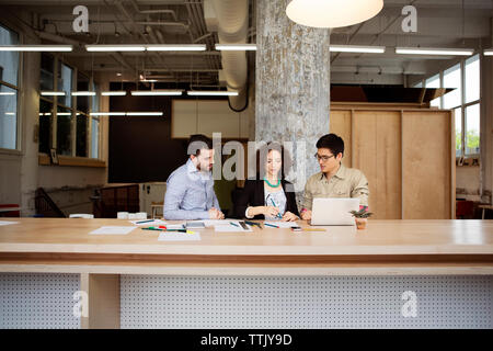 Side view of business people using laptop computer while sitting at table in office Stock Photo