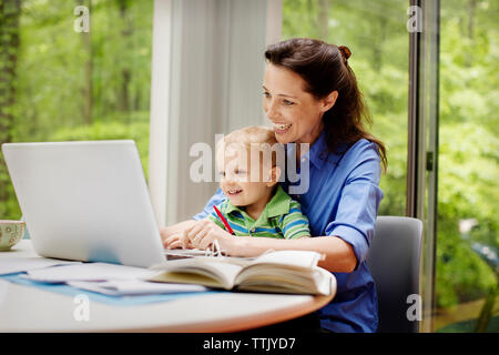 Happy mother with son using laptop at table against window Stock Photo