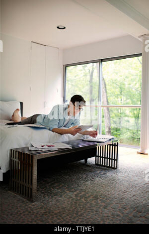 Man using tablet computer while working on bed at home Stock Photo