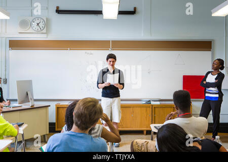 Teacher looking at student reading paper during in lesson in classroom Stock Photo
