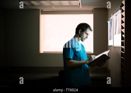 Doctor writing report while standing in hospital ward Stock Photo