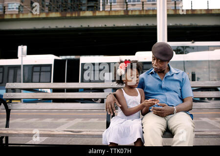 Granddaughter talking to grandfather while sitting on bench in city Stock Photo