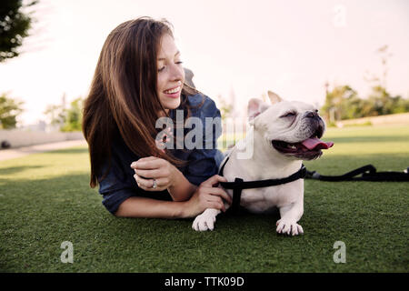 Happy woman lying with dog on grassy field at park Stock Photo