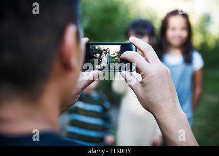 Cropped image of man photographing children while standing in orchard Stock Photo
