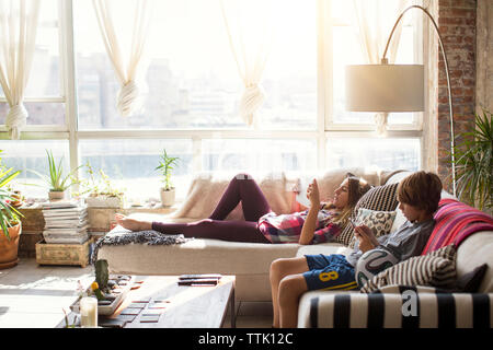 Siblings using technologies while relaxing in living room Stock Photo