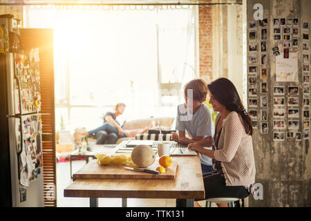Mother and son looking at laptop computer while father playing with daughter in backgrounds Stock Photo