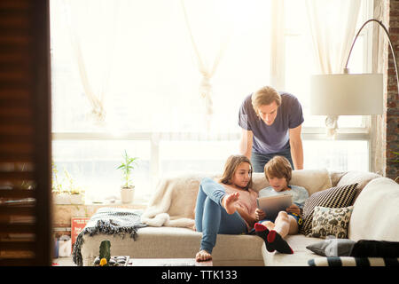 Father looking at children using tablet computer at home Stock Photo