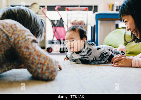Happy mother and grandfather playing with cute baby boy lying on rug at home Stock Photo