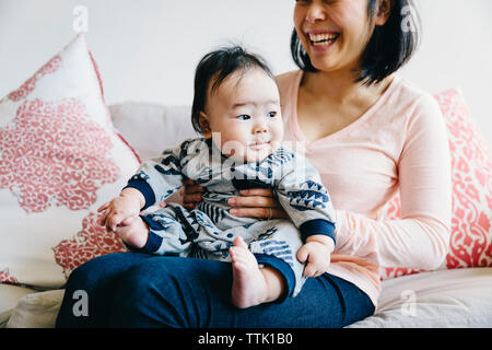 Midsection of happy mother holding cute son while sitting on sofa at home Stock Photo