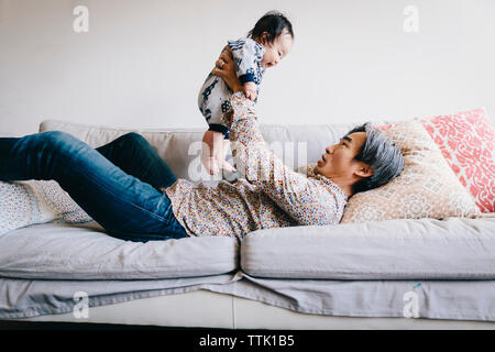 Grandfather playing with happy grandson while lying on sofa at home Stock Photo