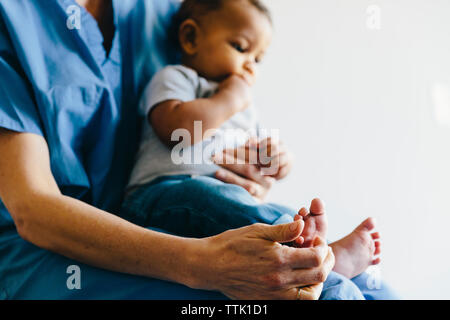 Midsection of female doctor holding baby boy while sitting against white background Stock Photo