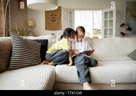 Sister looking at brother using tablet computer while sitting on sofa in living room Stock Photo