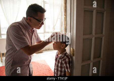 Father measuring son's height while standing at doorway in house Stock Photo