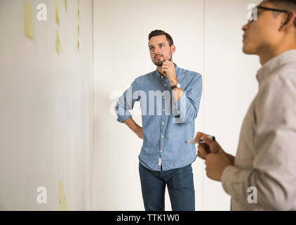business people discussing over sticky notes while standing against white wall in creative office Stock Photo
