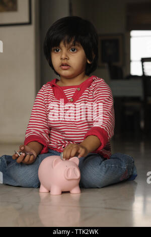 Indian girl putting coin into a piggy bank with her father and brother ...
