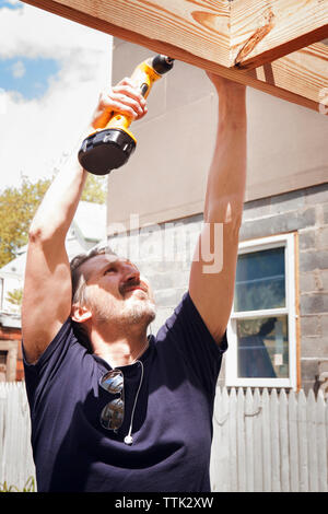 Carpenter drilling wooden plank while standing in yard Stock Photo