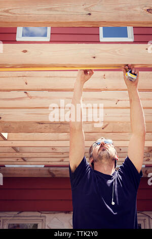 Man measuring plank while standing in yard Stock Photo