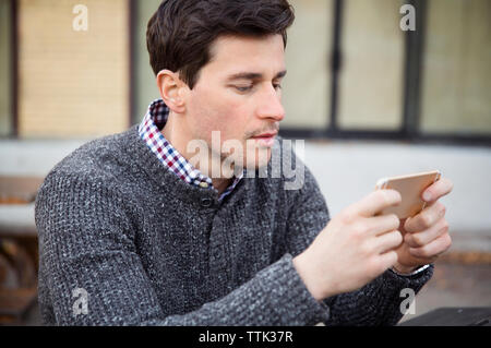 Man using mobile phone while sitting outdoors Stock Photo