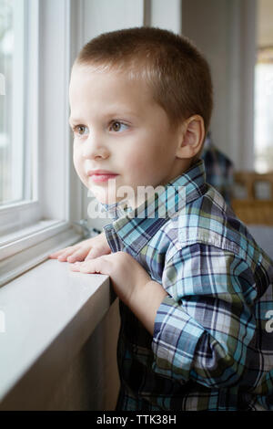 Smiling boy looking through window while standing at home Stock Photo