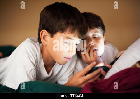 Brothers looking in phone while resting on bed at home Stock Photo