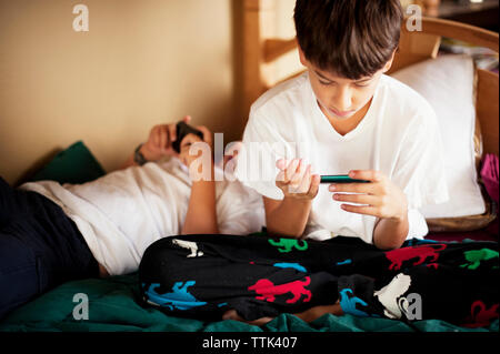 Brothers using phone while resting on bed at home Stock Photo