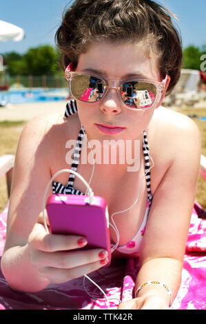 Woman wearing sunglasses using phone while lying at beach on sunny day Stock Photo