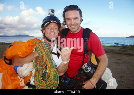 Portrait of smiling friends with parachute standing on field against sea Stock Photo
