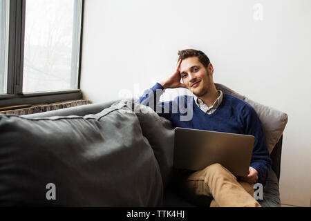Smiling man using laptop while sitting on sofa at home Stock Photo