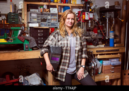 Portrait of confident female mechanic holding protective mask in workshop Stock Photo