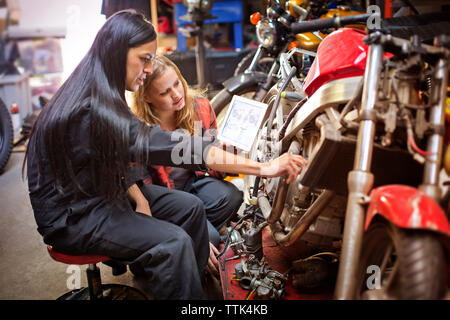 Female mechanics using digital tablet while repairing bike in workshop Stock Photo