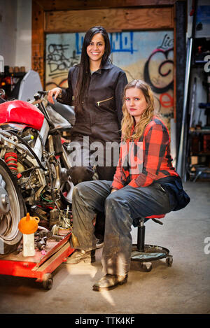 Portrait of confident female mechanics by bike in workshop Stock Photo