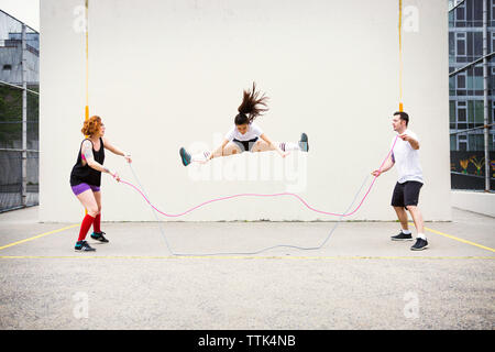 Confident friends performing double Dutch on street against wall Stock Photo
