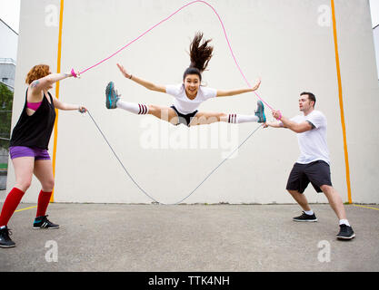 Confident woman doing splits while performing double Dutch against wall Stock Photo