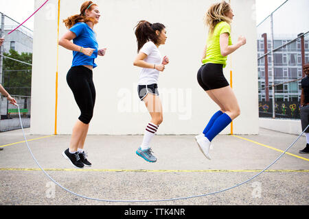 Side view of women performing double Dutch against wall Stock Photo