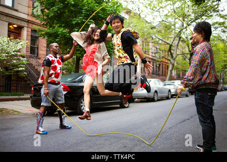 Friends enjoying double Dutch on street against parked cars Stock Photo