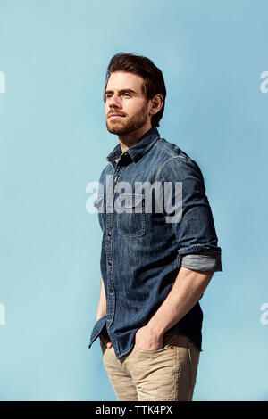 Handsome man with hands in pockets standing against blue background Stock Photo