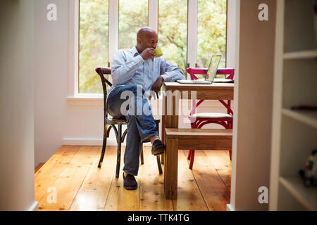 Senior man using laptop while drinking coffee at home Stock Photo